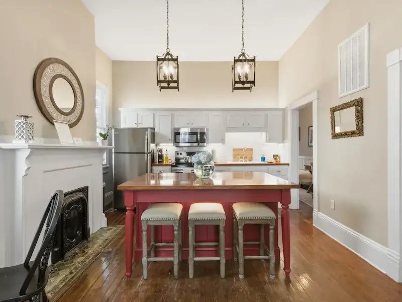 Suite 314A fully stocked kitchen at The Wilder House â€” signature maroon island with bar stools globe pendant lights and heart-pine floors